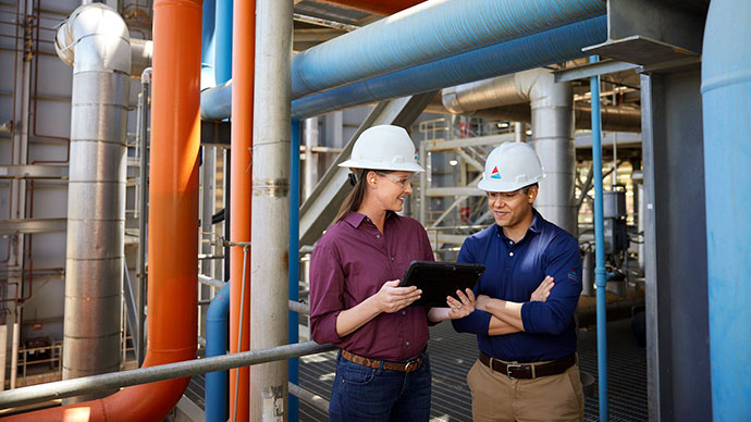 Woman and man plant operators smiling and looking at tablet